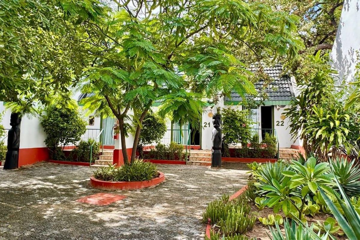 A view of the hotel courtyard featuring landscaped garden beds, mature trees, and paved walkways leading to guest room entrances.