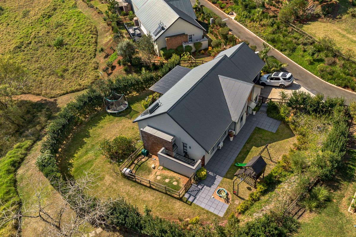 Aerial view of a townhouse property featuring a metal roof, paved patio area, and a well-maintained garden with perimeter fencing.