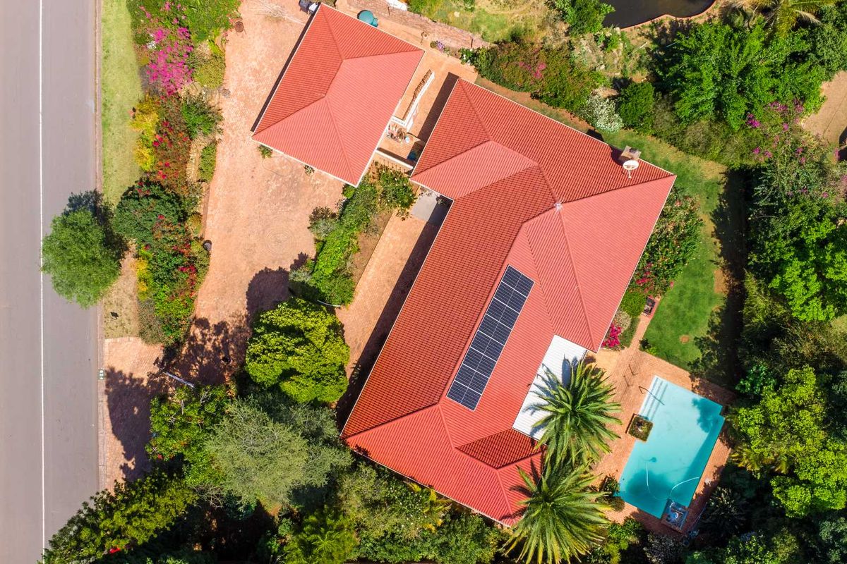Aerial view of the property featuring a tiled roof with solar panels, a swimming pool, and established garden surroundings.