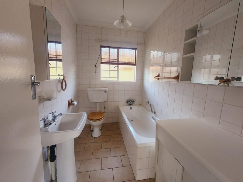 A functional bathroom featuring a pedestal basin, bathtub, toilet, and built-in vanity cabinet with classic tiled finishes.