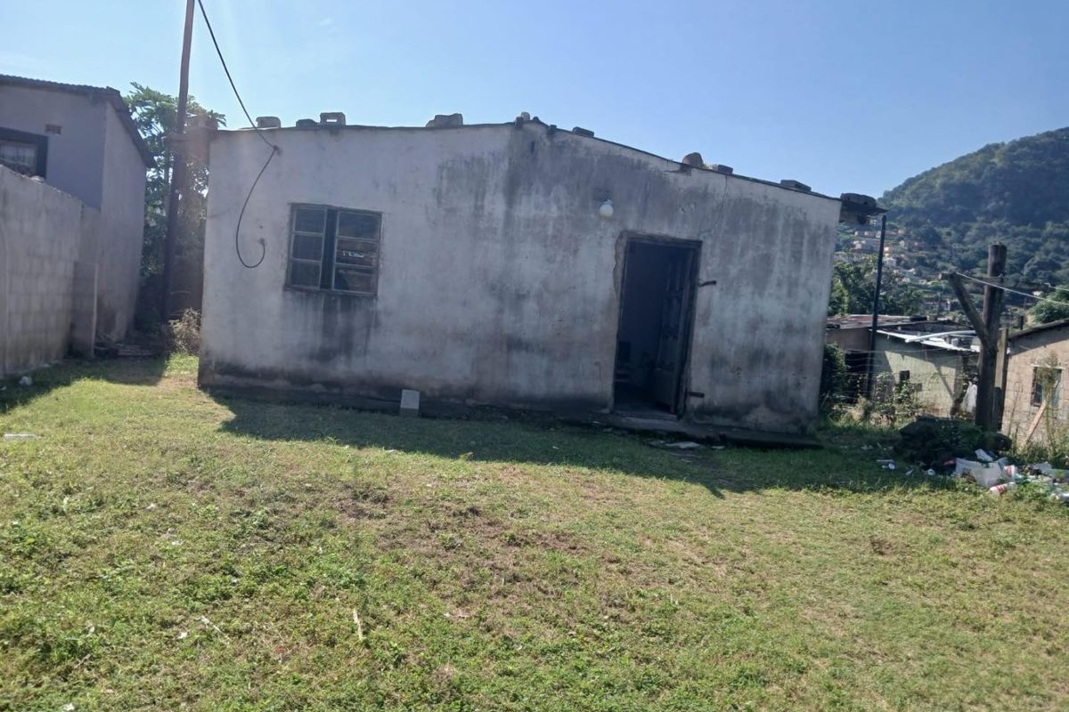 Rear view of a detached residential structure showing significant weathering and deterioration of the exterior walls and roofline.