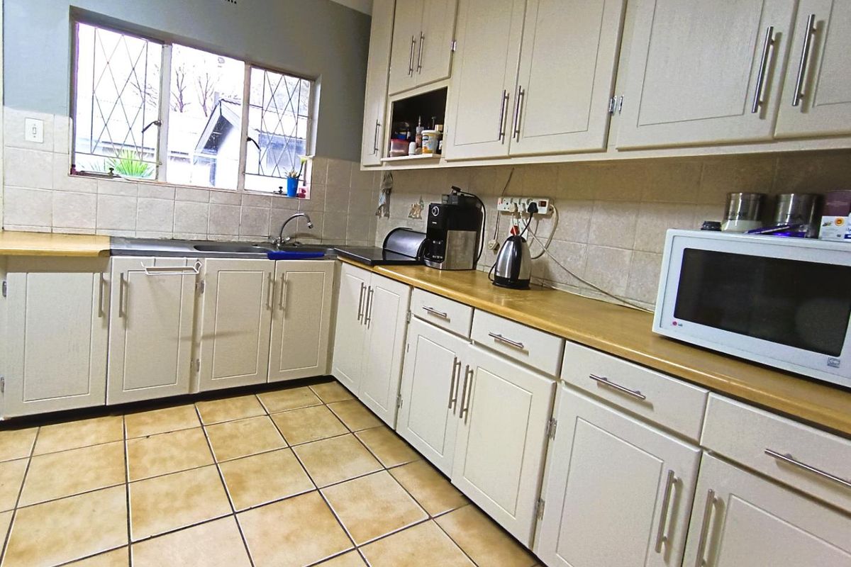 A functional kitchen featuring light-toned cabinetry, laminate countertops, tiled flooring, and a stainless steel sink with a window view.