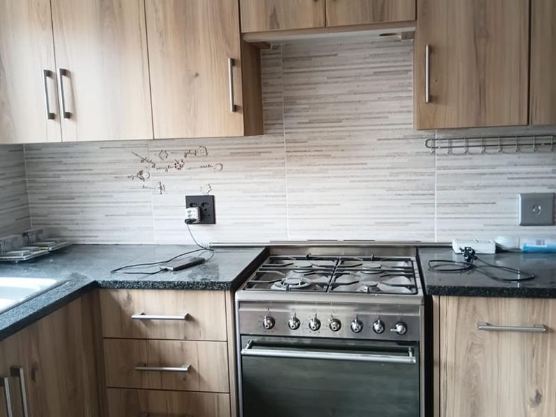 A functional kitchen featuring wood-look cabinetry, granite countertops, a tiled backsplash, and a stainless steel gas stove with an integrated oven.