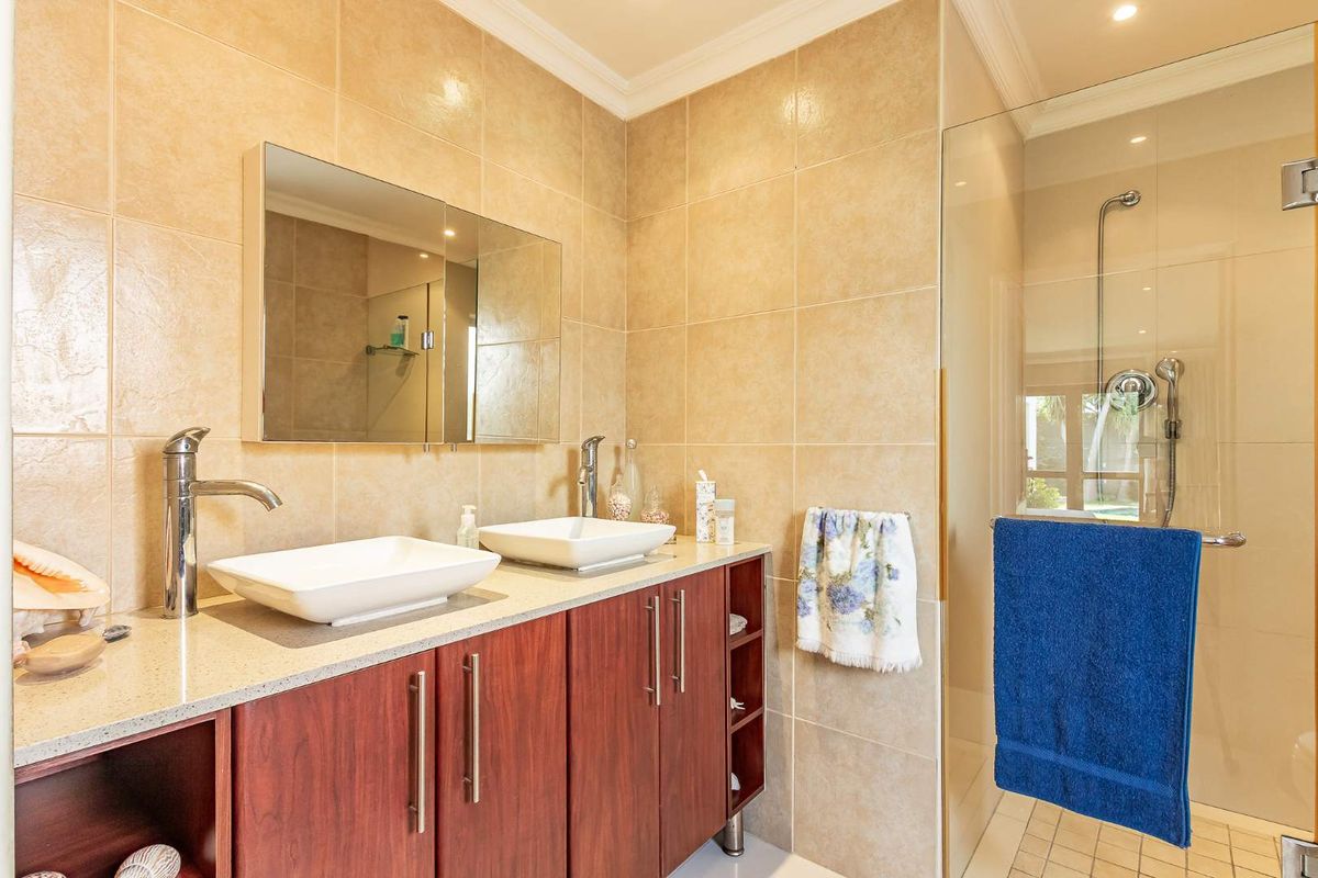 Modern bathroom featuring a double vanity with vessel sinks, stone countertop, wooden cabinetry, and a glass-enclosed walk-in shower with tiled walls.