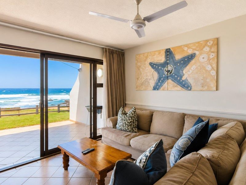 A bright living room featuring tiled floors, a ceiling fan, and large sliding glass doors that open onto a patio with ocean views.