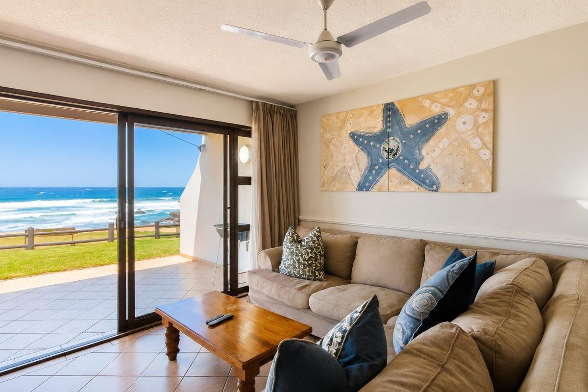 A bright living room featuring tiled floors, a ceiling fan, and large sliding glass doors that open onto a patio with ocean views.