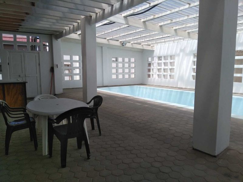 A covered indoor swimming pool area featuring a paved deck, structural columns, and decorative ventilation blocks, providing a functional space for year-round recreation.