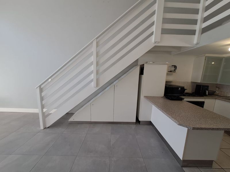 Open plan living area featuring a modern staircase with integrated under-stair storage and a functional kitchen with stone-look countertops and built-in appliances.