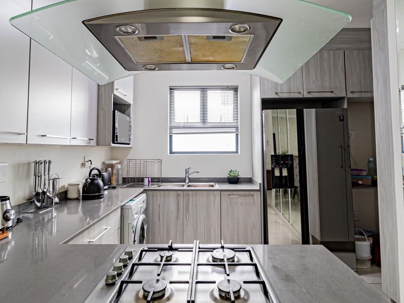 Modern kitchen featuring stone countertops, gas hob with overhead extractor, ample built-in cabinetry, and a functional double sink layout.