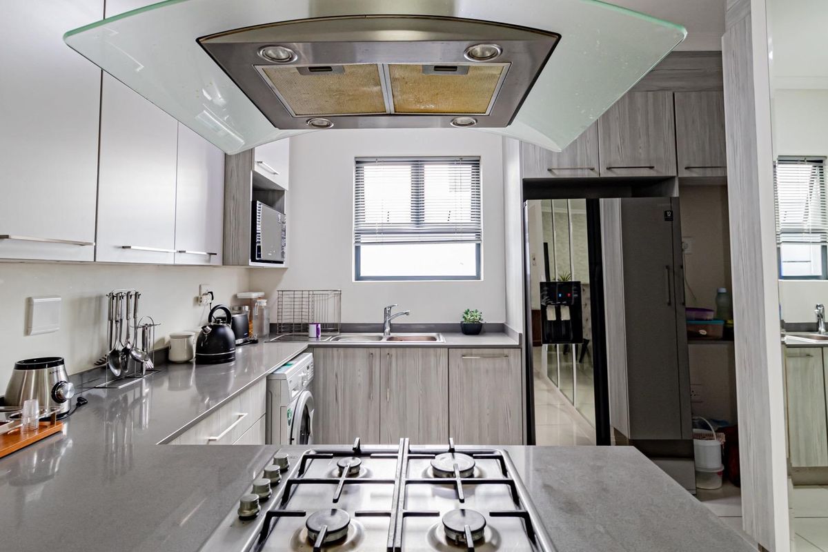 Modern kitchen featuring stone countertops, gas hob with overhead extractor, ample built-in cabinetry, and a functional double sink layout.