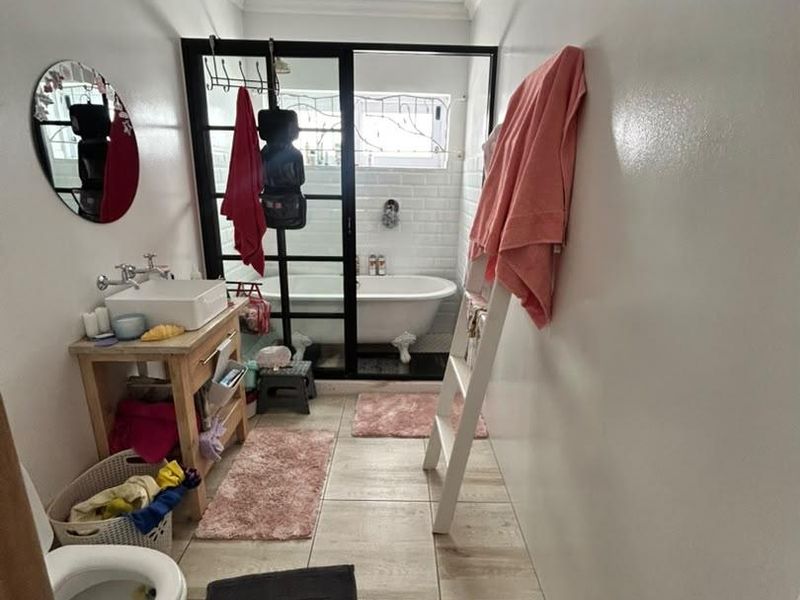 A modern bathroom featuring a freestanding bathtub, a black-framed glass shower enclosure, a vessel sink, and neutral tiled flooring.