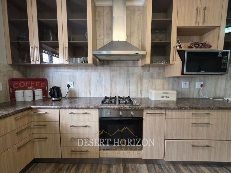 A functional kitchen featuring light wood-finish cabinetry, a gas hob, built-in oven, stainless steel extractor fan, and a tiled backsplash.