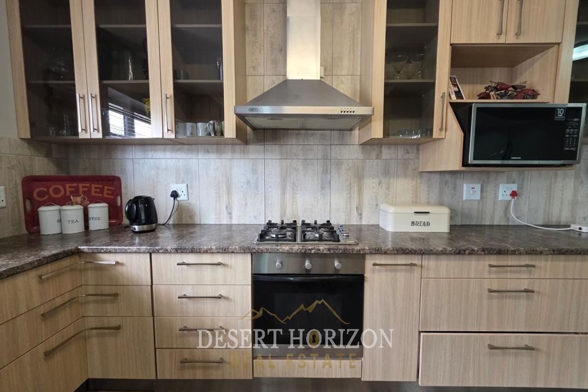A functional kitchen featuring light wood-finish cabinetry, a gas hob, built-in oven, stainless steel extractor fan, and a tiled backsplash.