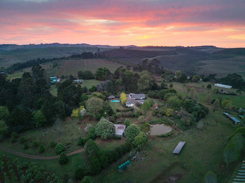 Aerial view of a sprawling farm property featuring a main residence, swimming pool, private dam, solar infrastructure, and extensive landscaped grounds at sunset.