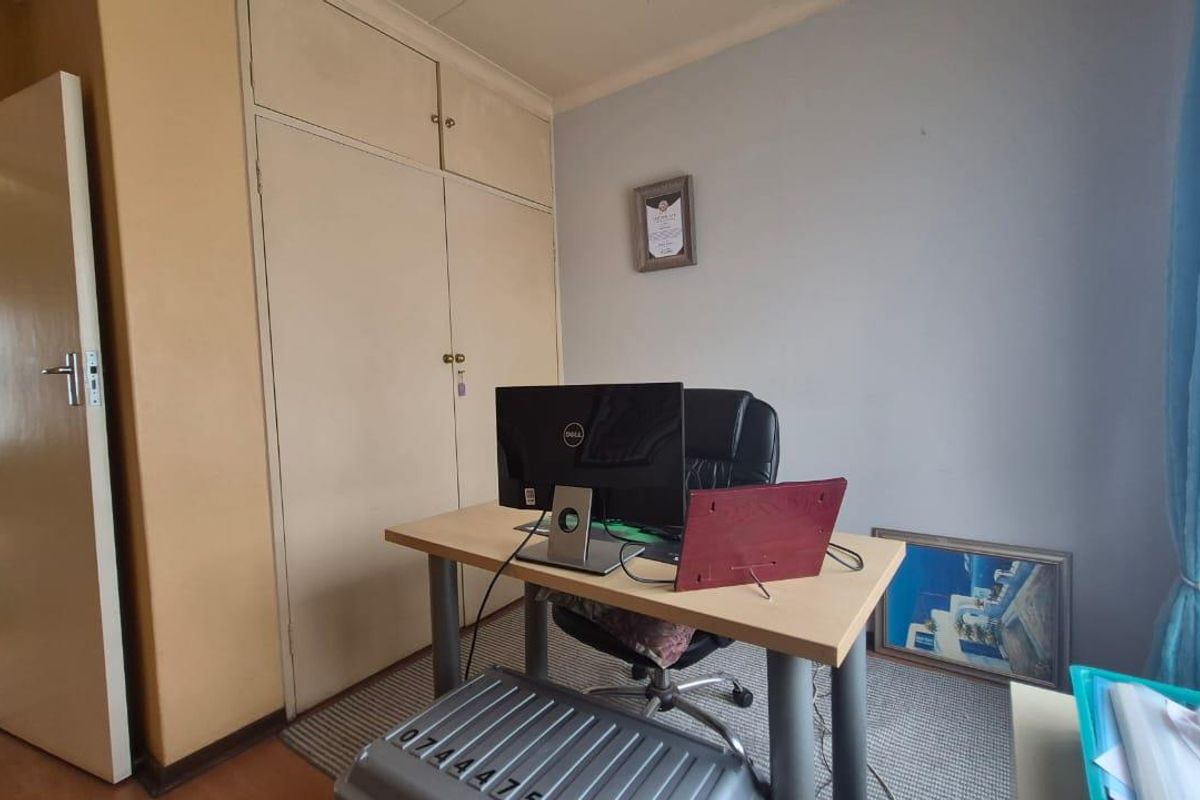 A bedroom featuring built-in cupboards and neutral wall finishes, currently utilized as a home office space.