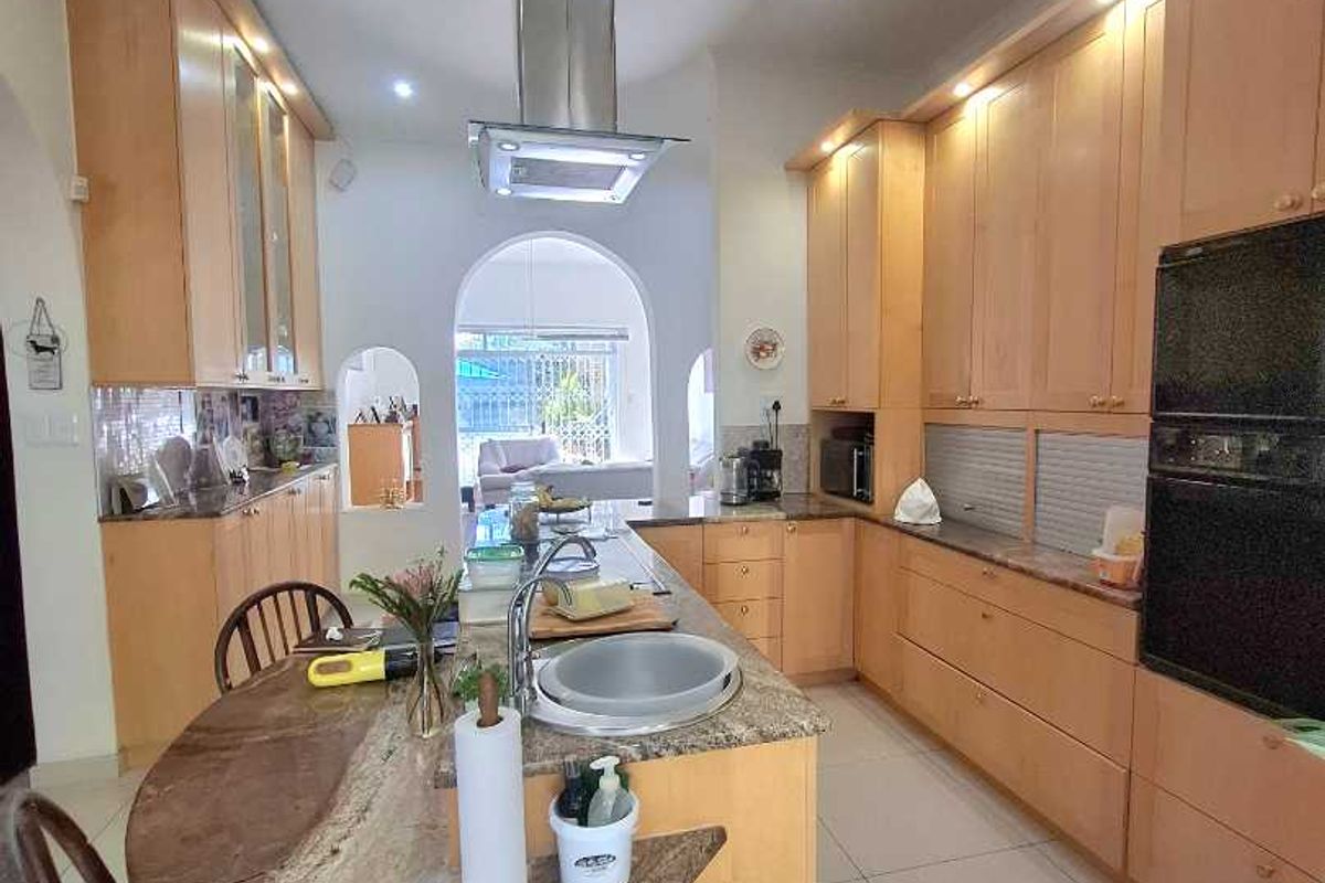 A functional kitchen featuring light wood cabinetry, granite countertops, a central island with integrated sink, and built-in stainless steel appliances.