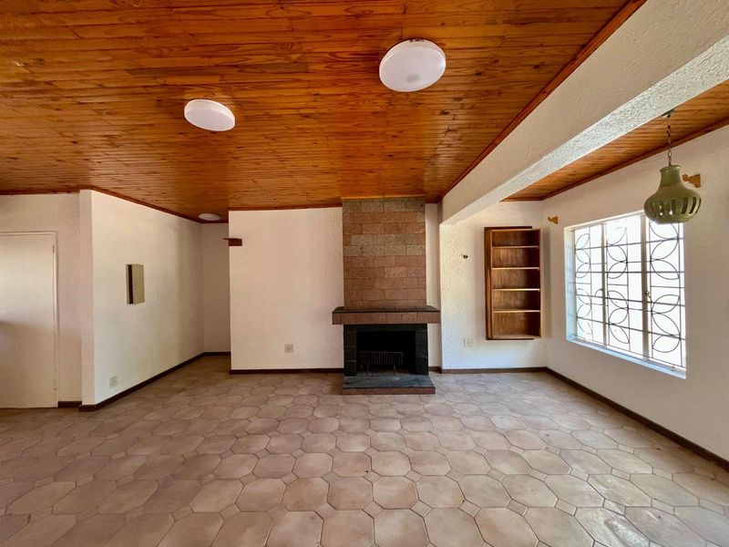 Spacious living room featuring a brick fireplace, timber ceiling, and tiled flooring, offering a blank canvas for renovation.