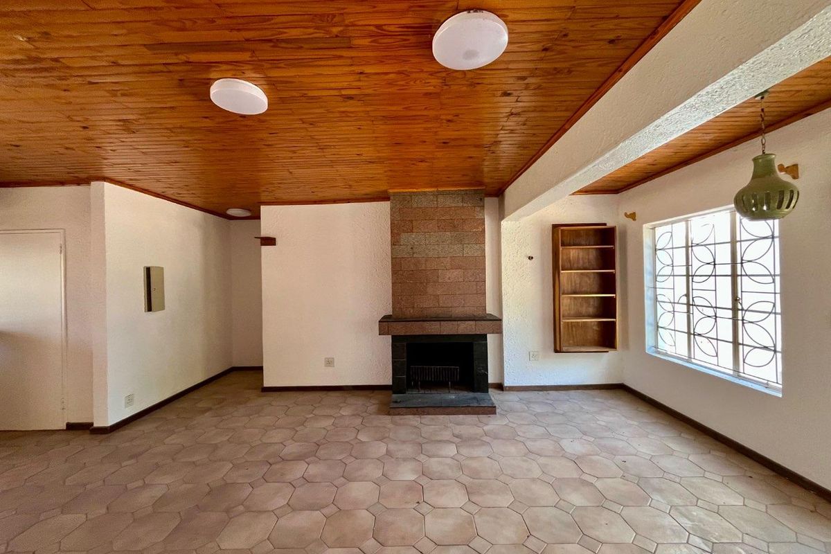 Spacious living room featuring a brick fireplace, timber ceiling, and tiled flooring, offering a blank canvas for renovation.