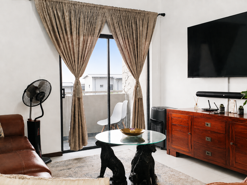 A well-lit living room featuring tiled flooring and a sliding glass door that provides access to an outdoor balcony area.