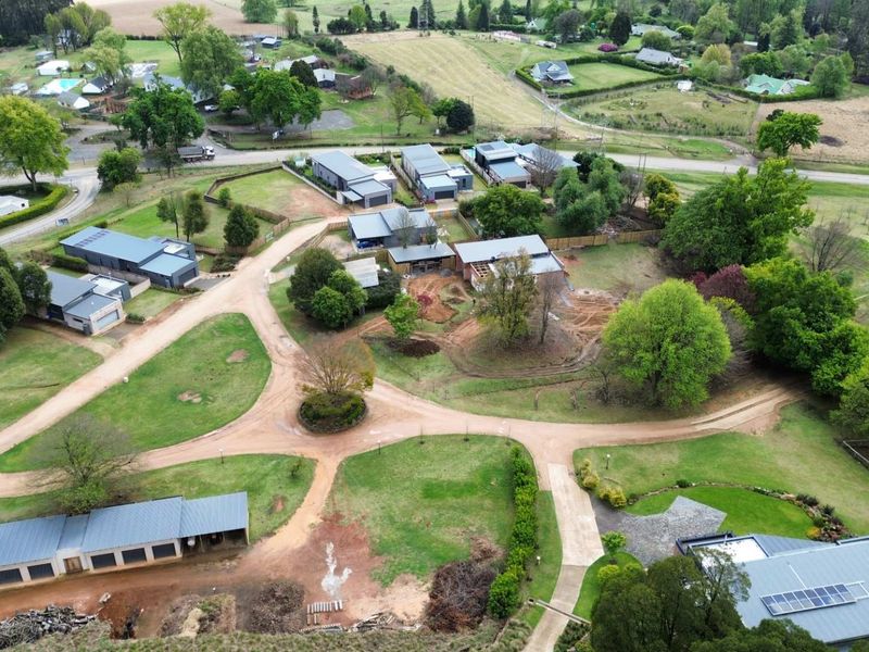 An aerial view of a residential estate featuring multiple dwellings, gravel access roads, established trees, and landscaped grounds.