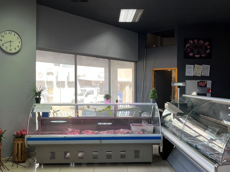 A commercial retail space featuring refrigerated display counters, tiled flooring, and large glass windows, suitable for a butcher shop or food retail business.