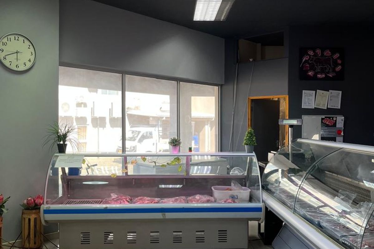 A commercial retail space featuring refrigerated display counters, tiled flooring, and large glass windows, suitable for a butcher shop or food retail business.