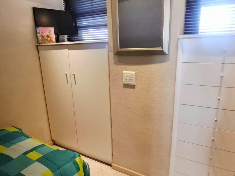 A compact bedroom featuring built-in storage cupboards, white drawer units, and venetian blinds, providing functional storage solutions within the space.