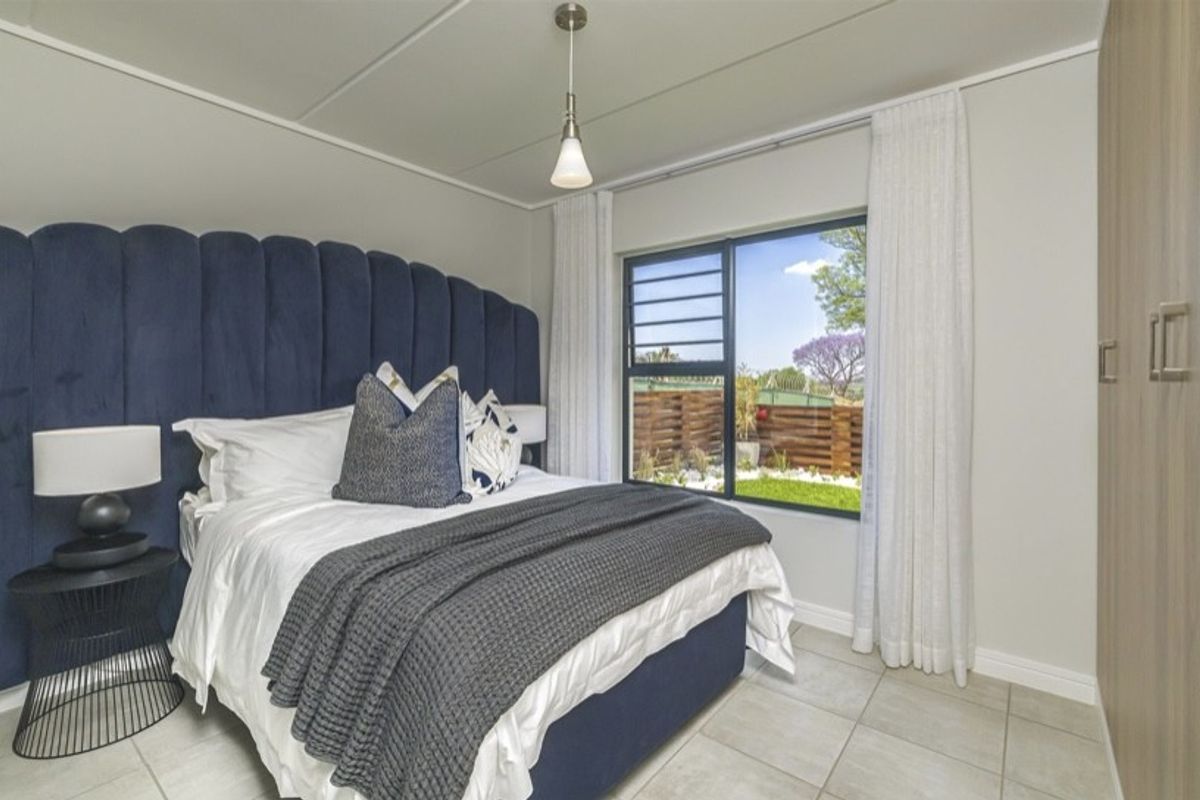 A well-maintained bedroom featuring tiled flooring, a built-in wardrobe, and a large window providing natural light and garden views.