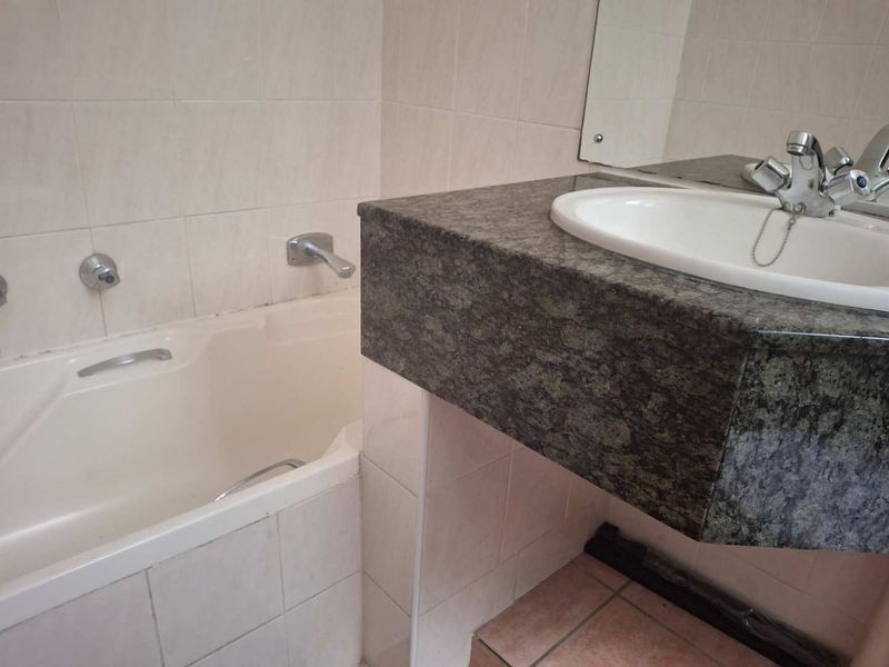 A functional bathroom featuring a built-in bathtub, granite vanity countertop with a drop-in sink, and neutral ceramic wall tiling.