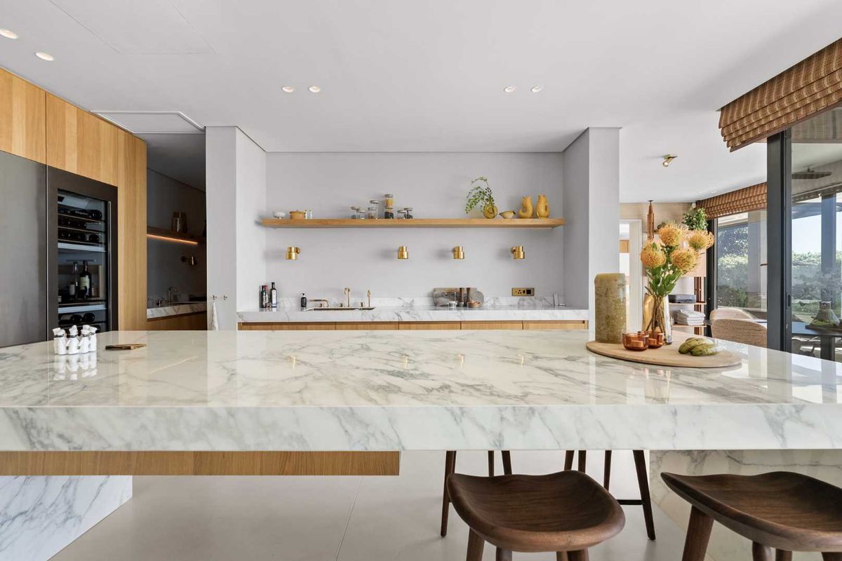 Modern luxury kitchen featuring a large marble island, integrated wine fridge, custom timber cabinetry, and floating shelves with high-end finishes.