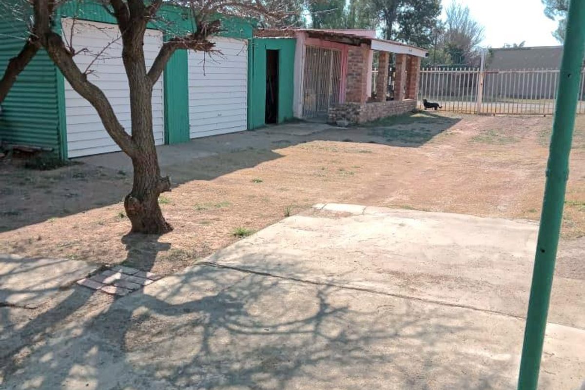 Rear exterior view featuring a corrugated metal garage, concrete driveway, and a covered patio area with brick pillars.