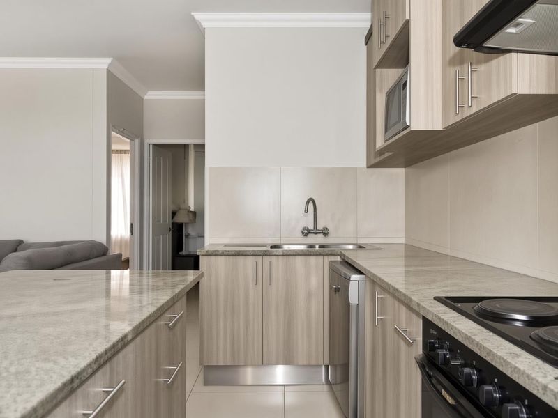 Modern kitchen featuring light wood-grain cabinetry, stone countertops, integrated appliances, and a functional layout with a breakfast bar.