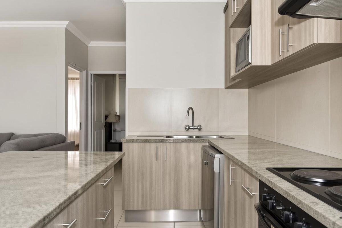 Modern kitchen featuring light wood-grain cabinetry, stone countertops, integrated appliances, and a functional layout with a breakfast bar.