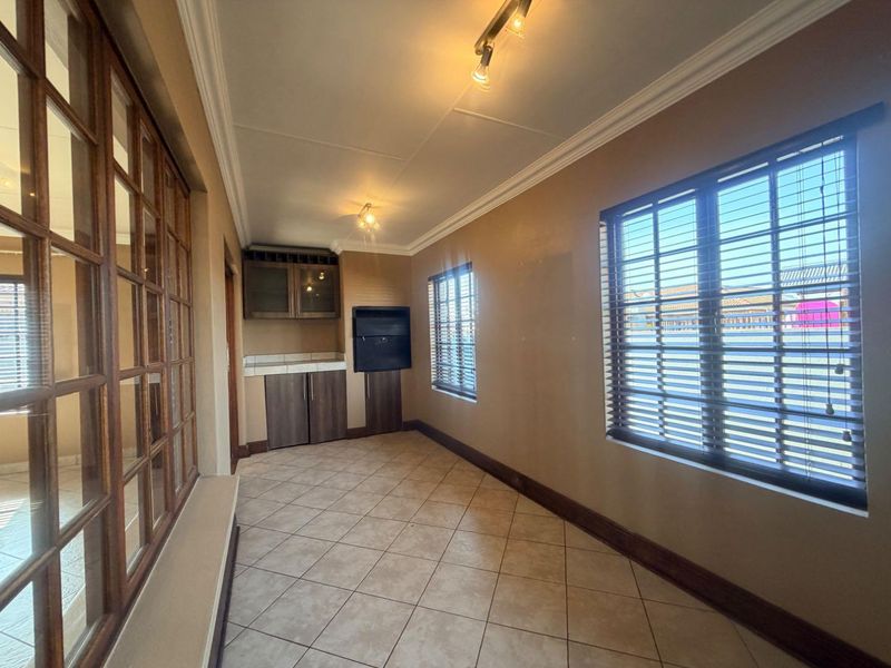 An empty living area featuring tiled floors, crown molding, built-in cabinetry, and a built-in braai, offering a versatile space for relaxation or entertainment.