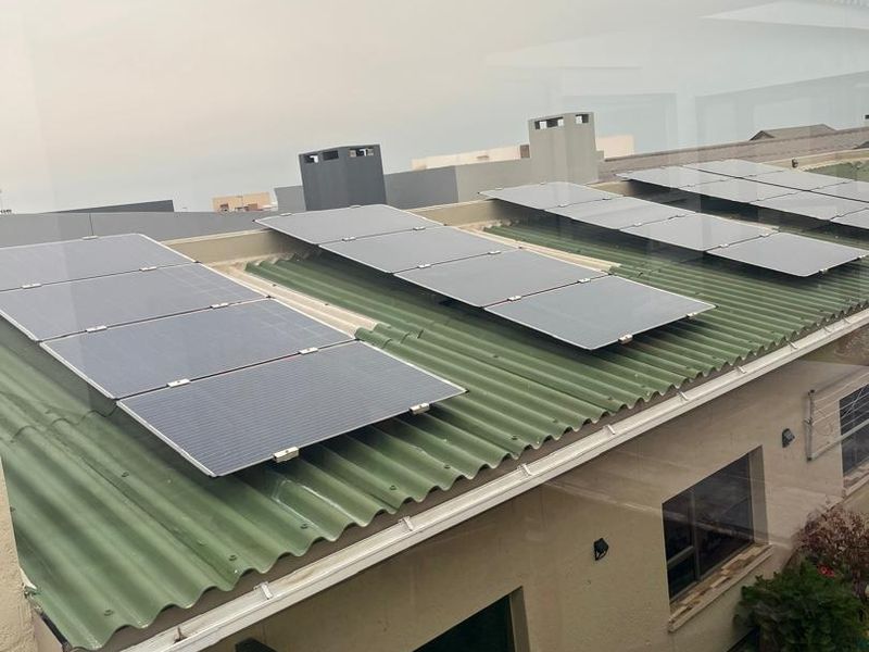 An elevated view of a residential roof featuring installed solar panels, corrugated roofing material, and integrated guttering systems.