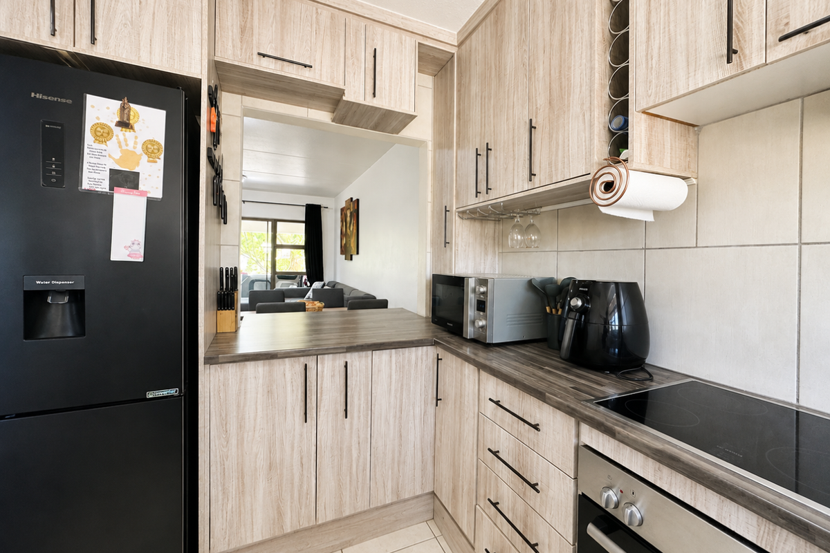 A well-maintained kitchen featuring light wood-grain cabinetry, dark laminate countertops, a built-in oven, electric hob, and a convenient pass-through window to the living area.