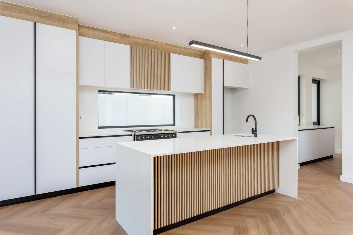 Modern, high-end kitchen featuring a central island with slatted timber detail, quartz countertops, integrated cabinetry, and premium herringbone timber flooring.