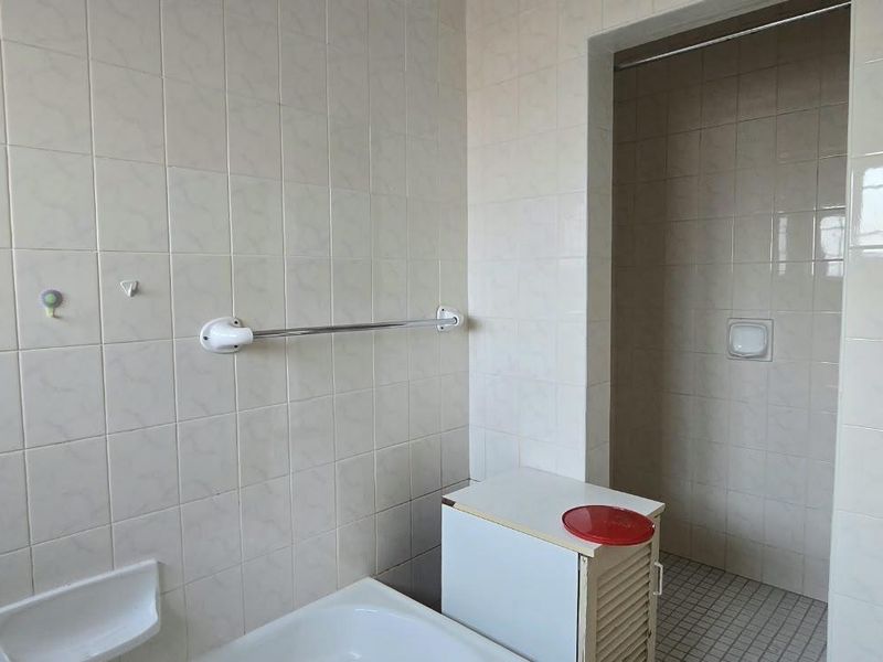 A dated bathroom featuring tiled walls and flooring, a built-in shower area, and basic fixtures, offering potential for a modern renovation.