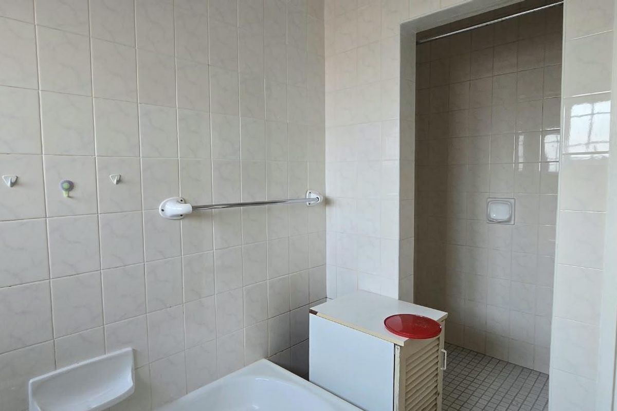 A dated bathroom featuring tiled walls and flooring, a built-in shower area, and basic fixtures, offering potential for a modern renovation.