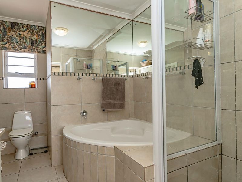 A functional bathroom featuring a corner bathtub, glass-enclosed shower, tiled finishes, and a wall-mounted mirror.