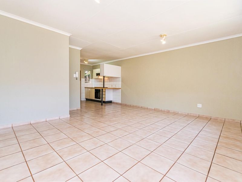 An open-plan living area featuring neutral tiled flooring and a compact, functional kitchen with built-in cabinetry and appliances.