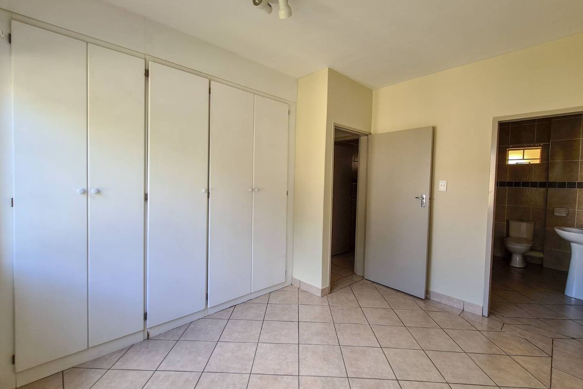 A vacant bedroom featuring built-in cupboards, tiled flooring, and direct access to an en-suite bathroom.