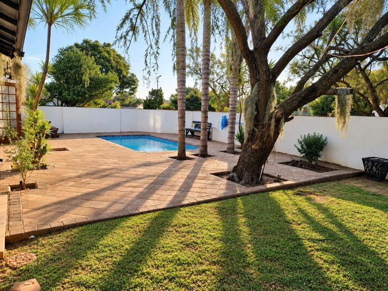 A private outdoor pool area featuring a paved patio, perimeter wall, and established trees, providing a functional space for relaxation and outdoor entertainment.