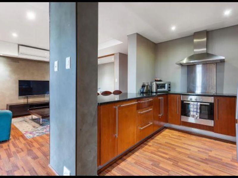 Open-plan living area featuring a modern kitchen with wooden cabinetry, granite countertops, built-in oven, and an adjacent lounge space with air conditioning.