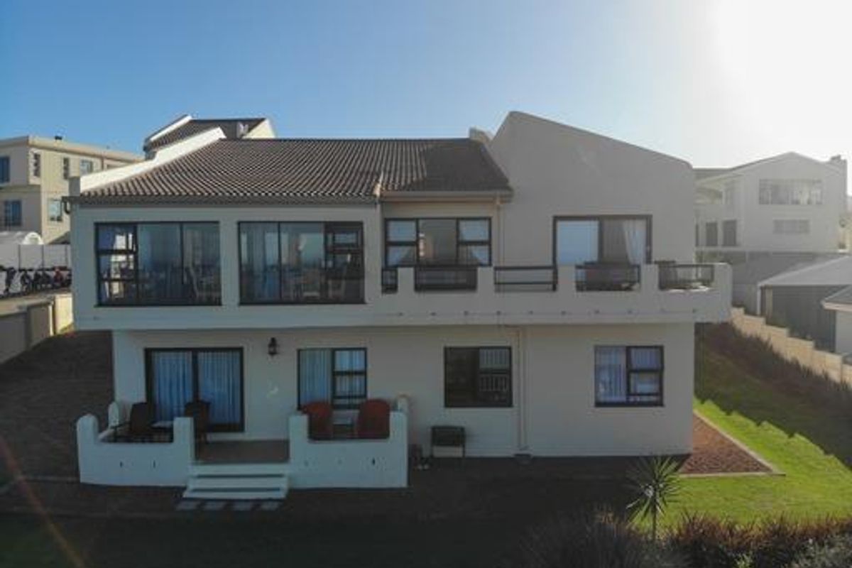 Rear elevation of a multi-story house featuring a tiled roof, upper-level balcony, ground-floor patio, and large aluminium-framed windows overlooking a garden.