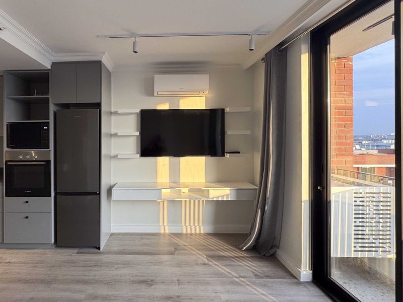 Modern open-plan living area featuring a sleek kitchen with built-in appliances, floating media console, split-system air conditioning, and large sliding doors leading to a balcony.