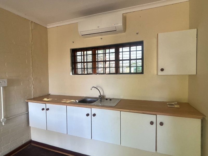 A compact kitchen area featuring basic cabinetry, a stainless steel sink, and a wall-mounted air conditioning unit in a functional, dated space.