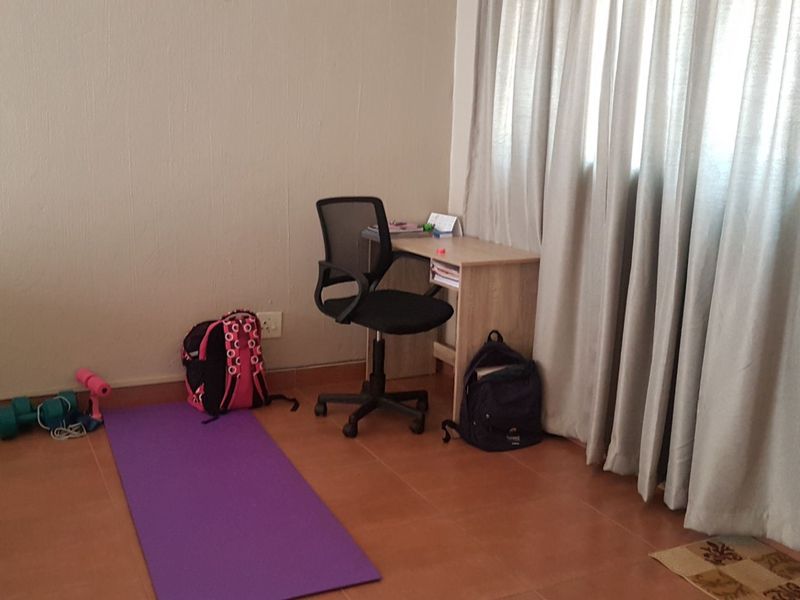 A simple bedroom featuring tiled flooring and window curtains, providing a functional space for rest or study.