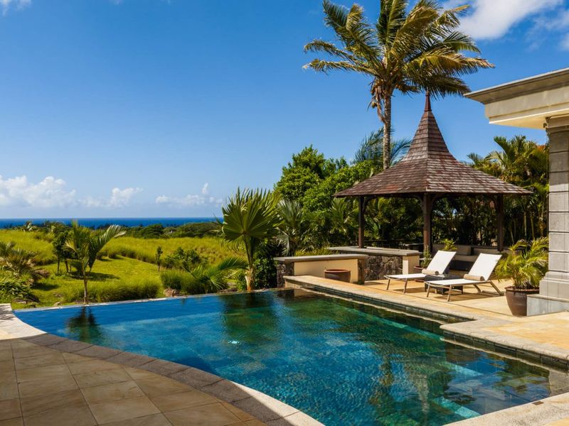 A stunning outdoor pool area featuring a tiled deck, a covered gazebo, and expansive views of the surrounding landscape and ocean.