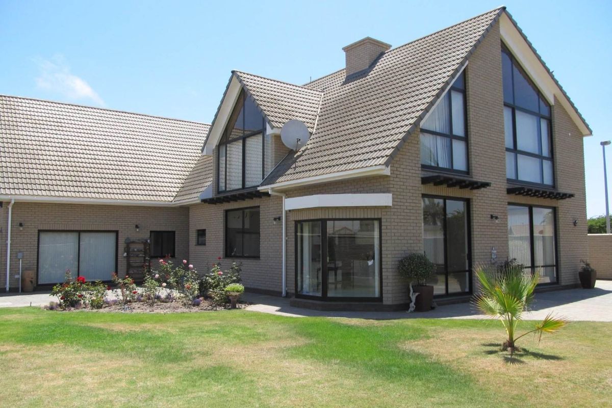 Rear view of a double-story brick house featuring a tiled roof, large windows, and a paved patio area overlooking the garden.